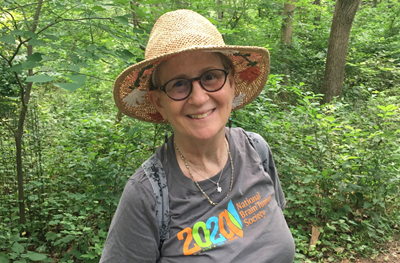 Lynn Oxenberg smiles while on a hike on a forest trail.